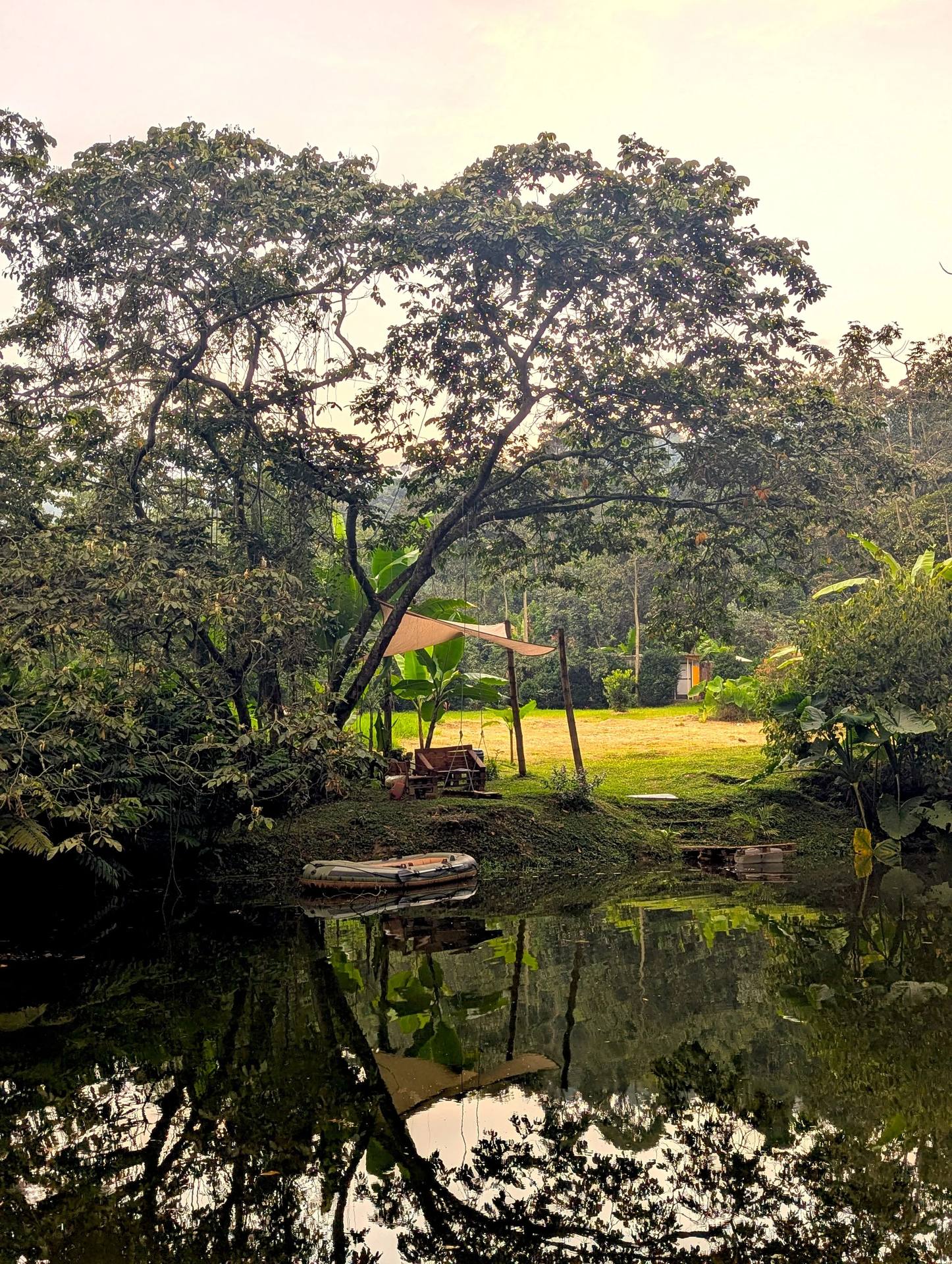 Paisaje con árboles, un río con reflejo y un bote inflable